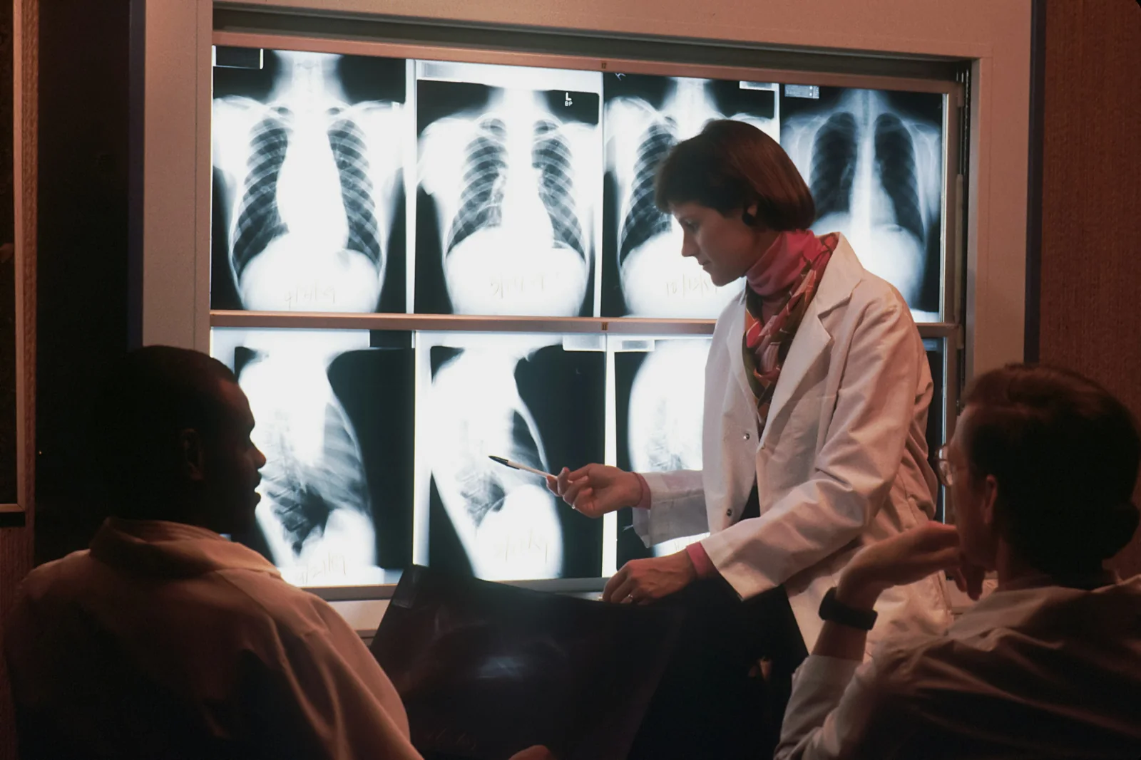 A clinician and patient speak in front of illuminated radiology images.