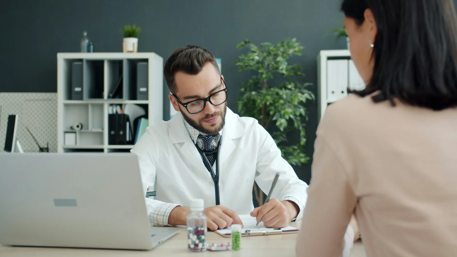 A clinician takes notes while speaking with a patient at a desk.