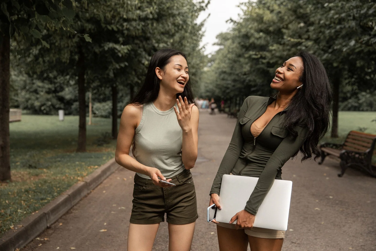 Two women stand together outdoors among leafy plants.
